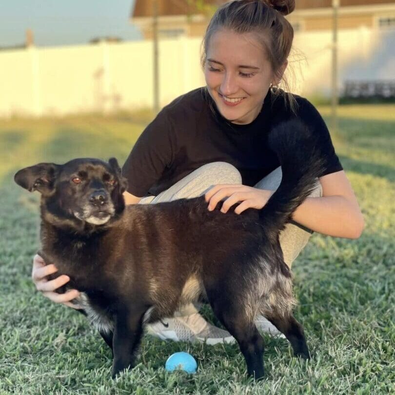 A woman is petting a dog on the grass.